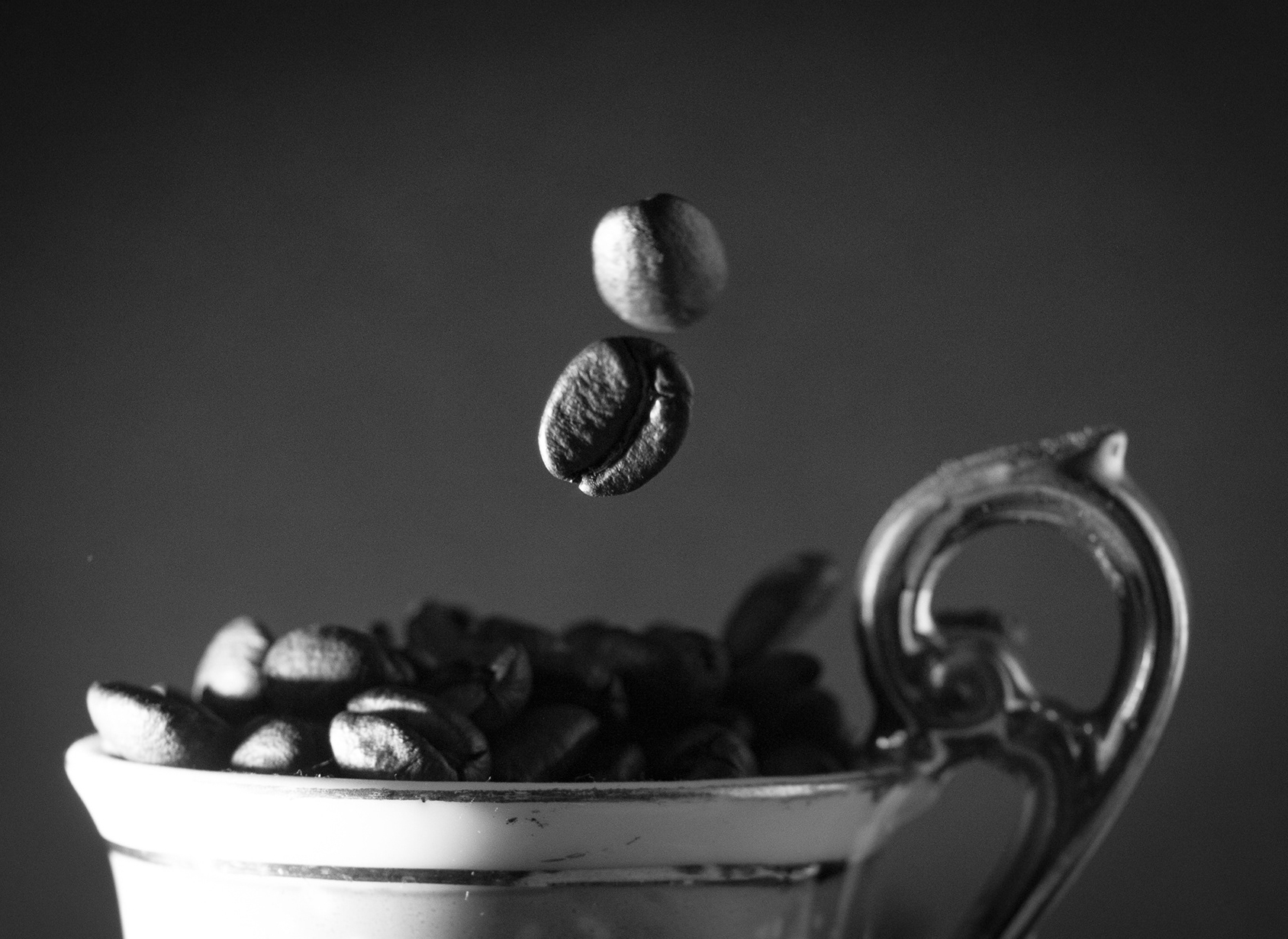 cup full of coffee beans with 2 beans falling into cup