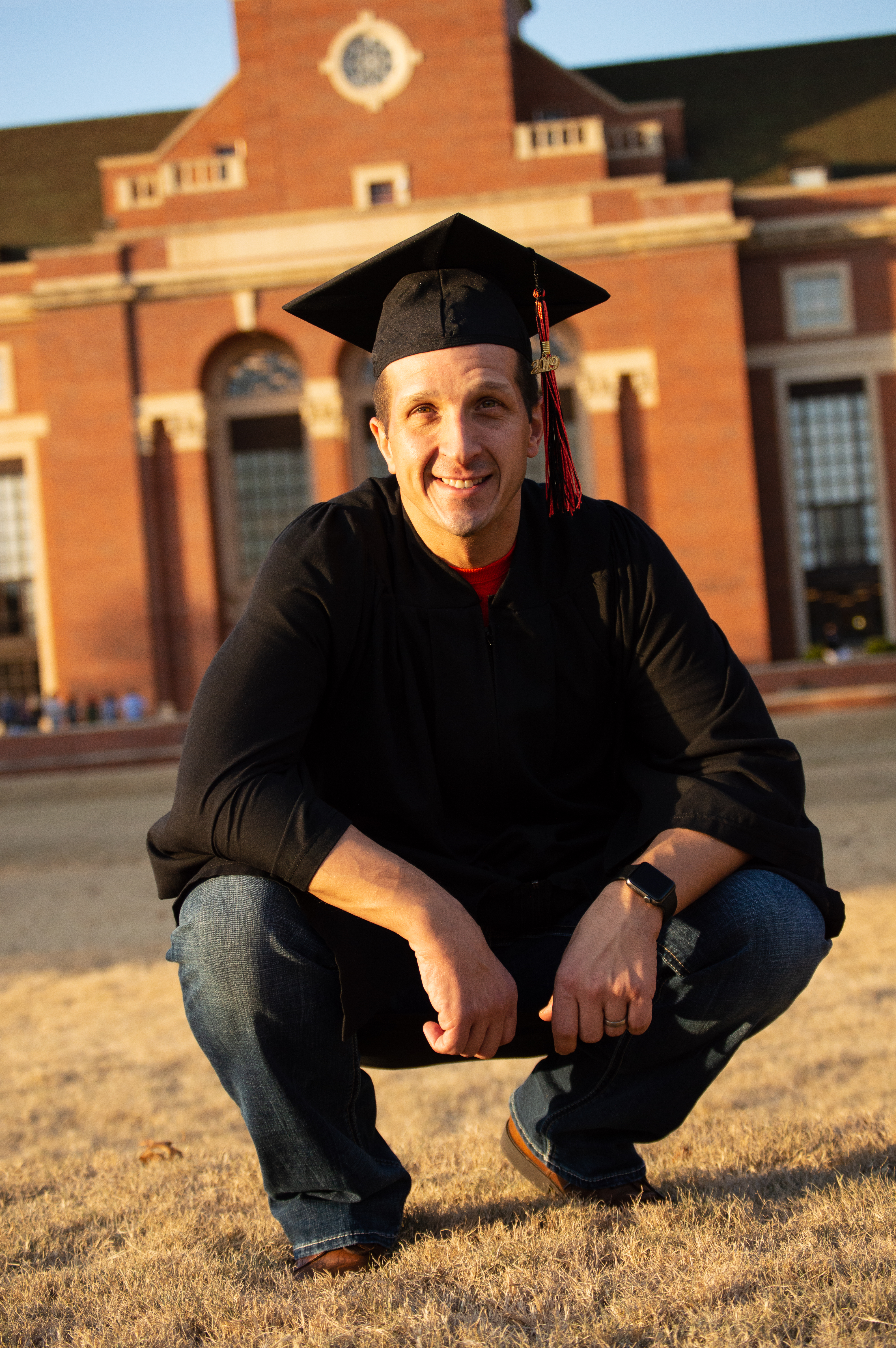young man squating down wearing graduation robe