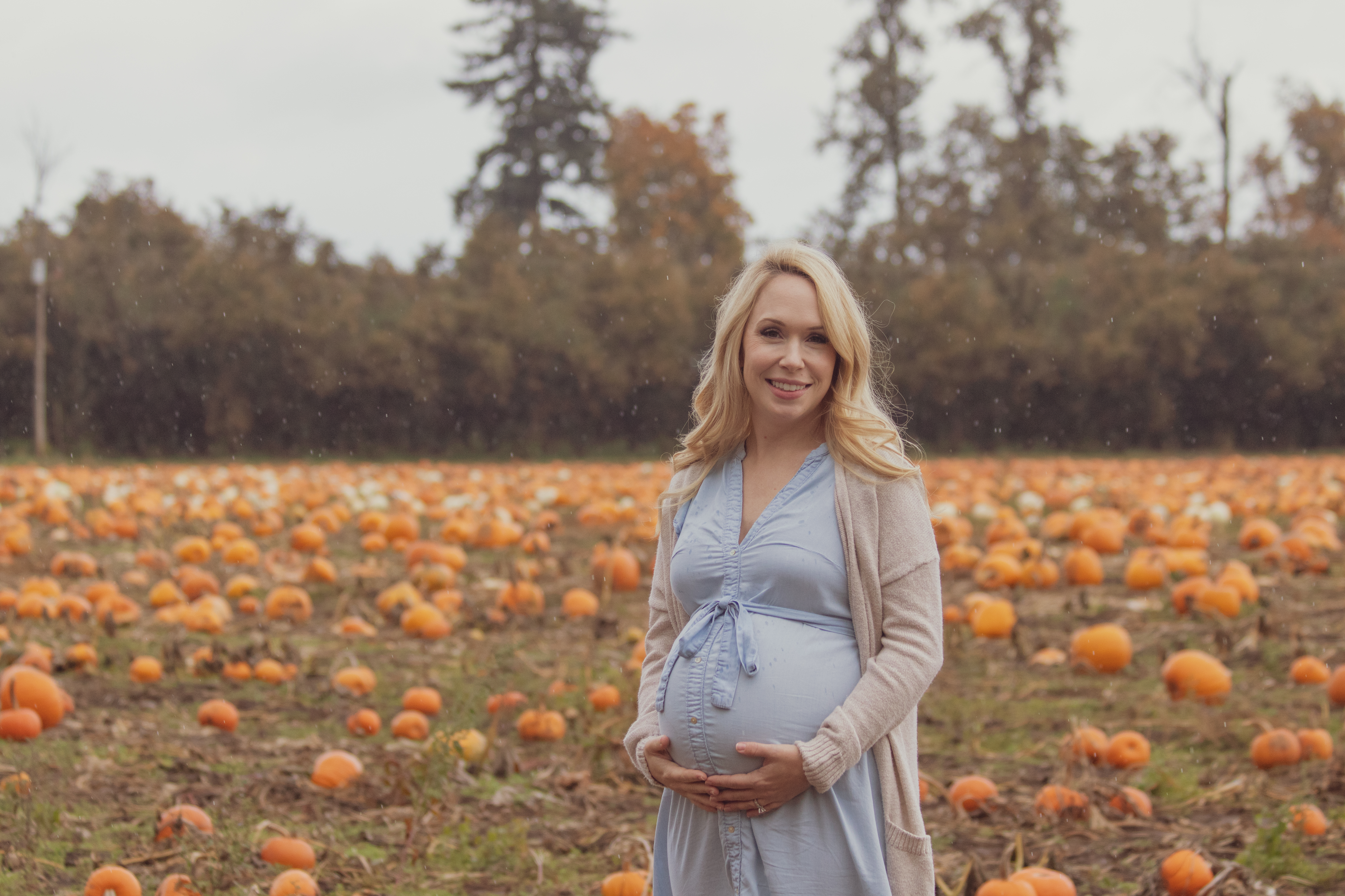 young woman posing in pumkin patch while holding baby bump