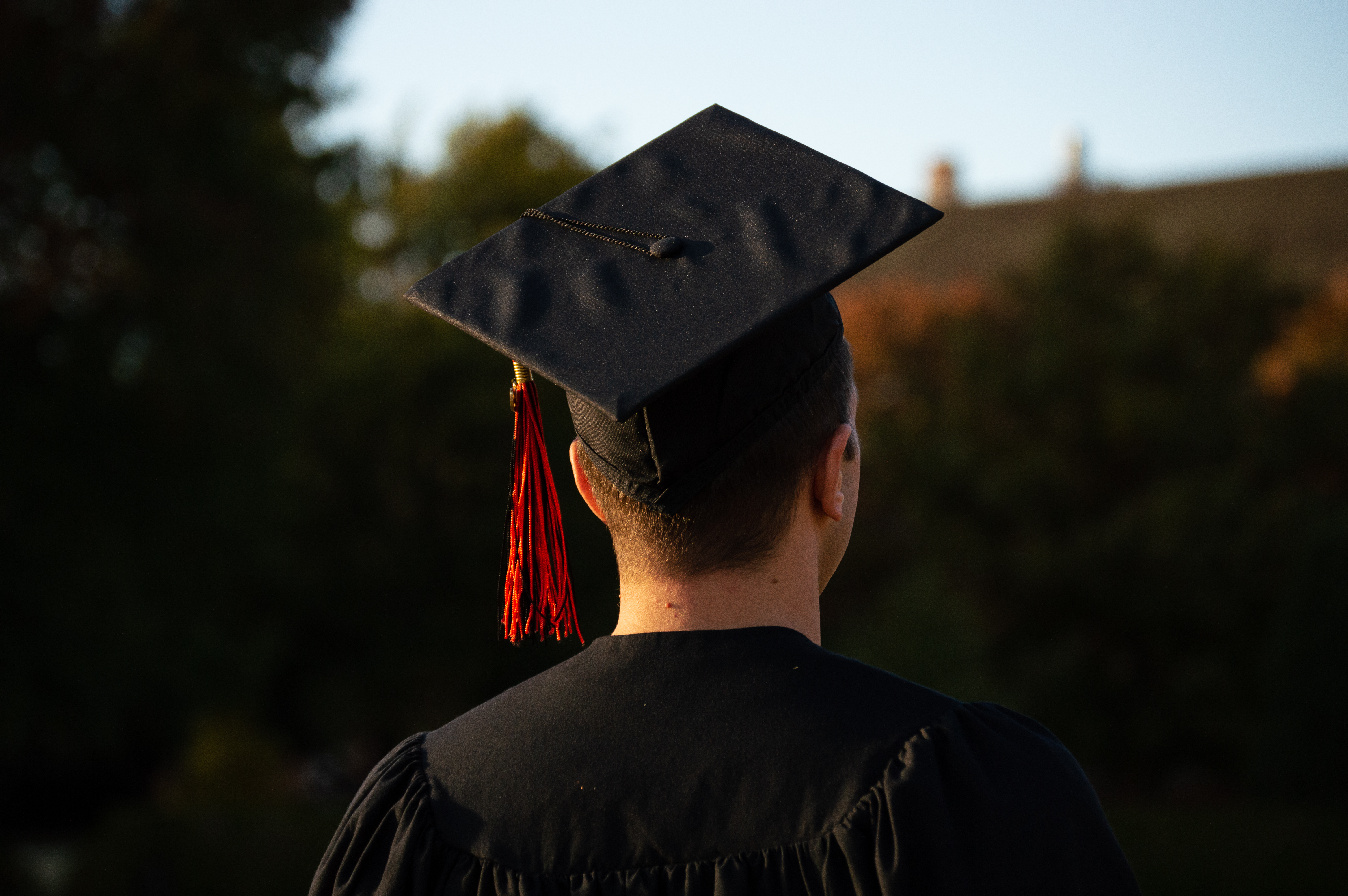 man walking away from camera wearing graduation robe and hat