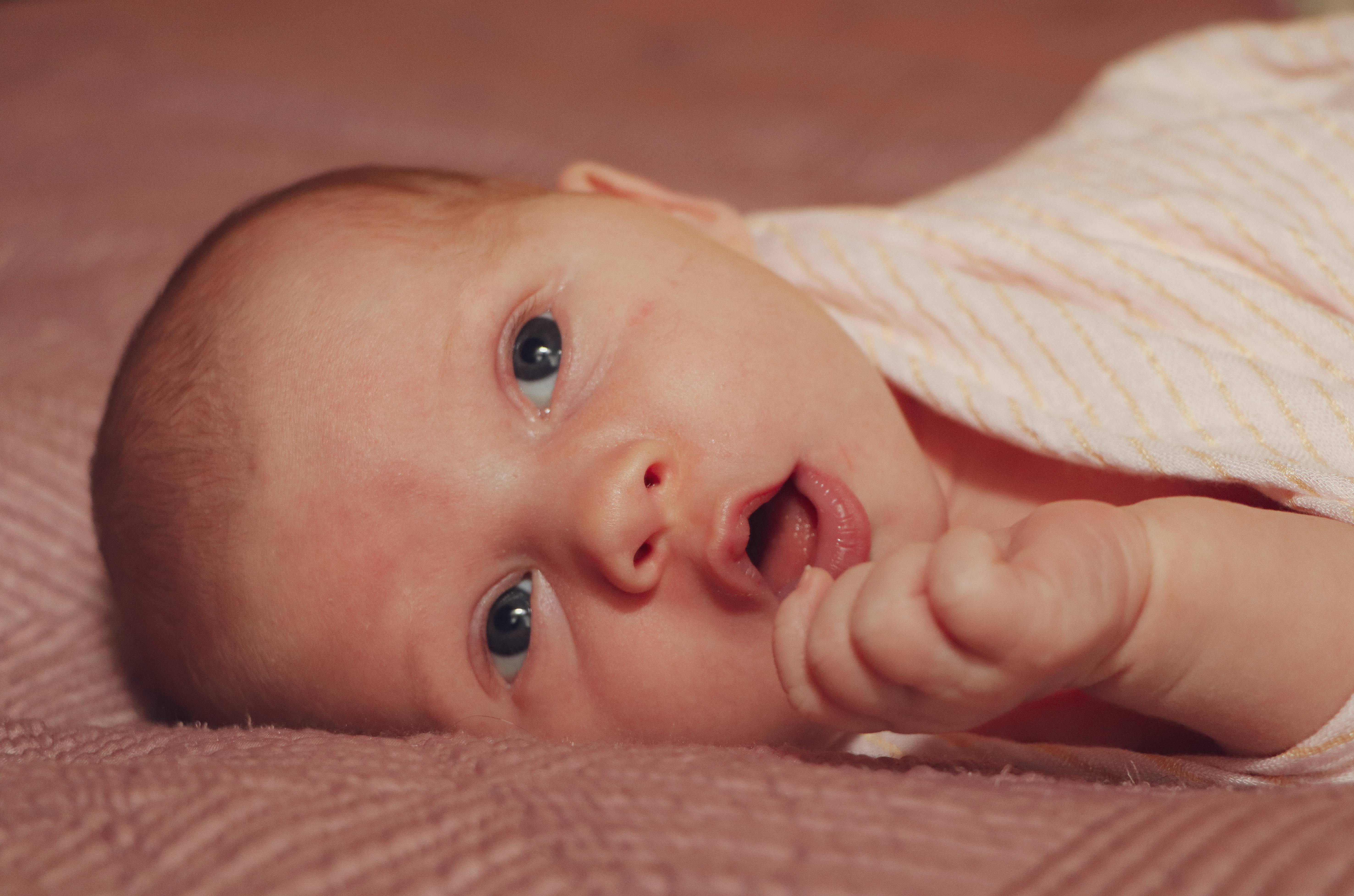 cutest baby ever laying on bed with mouth open with bright eyes